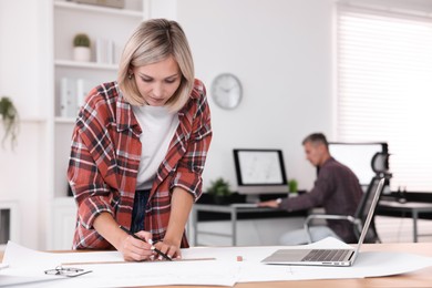 Architect making engineering drawing at table in office