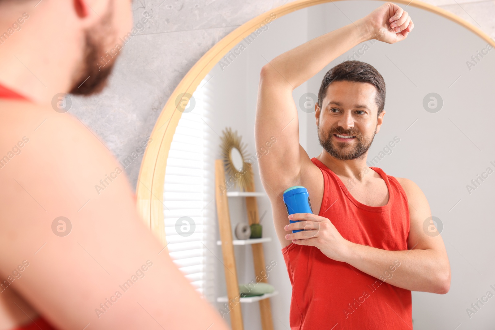 Photo of Smiling man applying solid deodorant near mirror at home