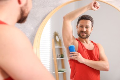 Smiling man applying solid deodorant near mirror at home