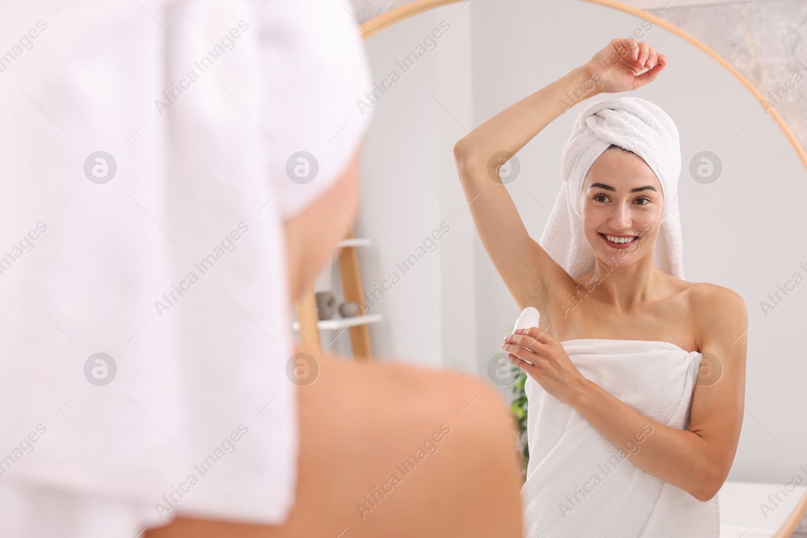 Photo of Smiling woman applying roll-on deodorant near mirror at home