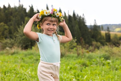 Photo of Portrait of smiling little girl in floral wreath at meadow. Child enjoying beautiful nature