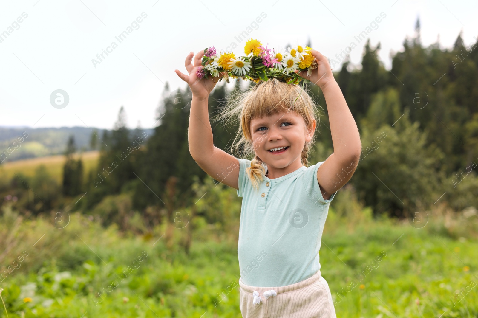 Photo of Portrait of smiling little girl with floral wreath at meadow. Child enjoying beautiful nature