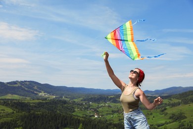 Smiling woman flying kite in mountains under blue sky. Space for text