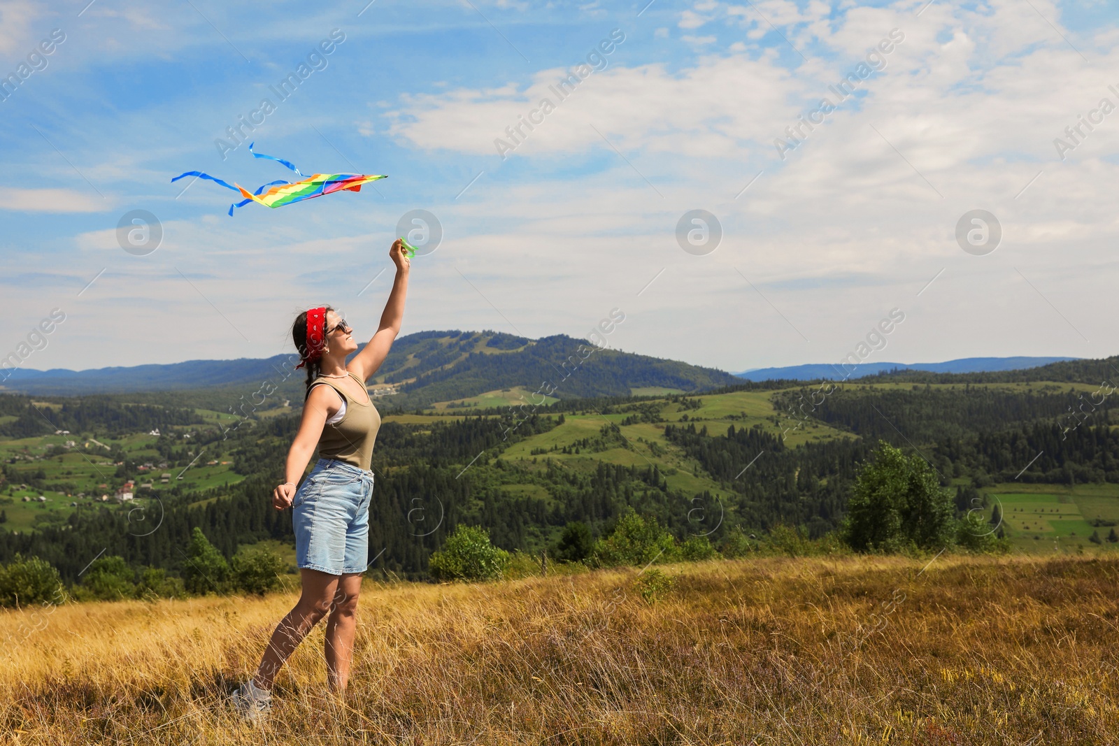 Photo of Smiling woman flying kite at field under blue sky. Space for text