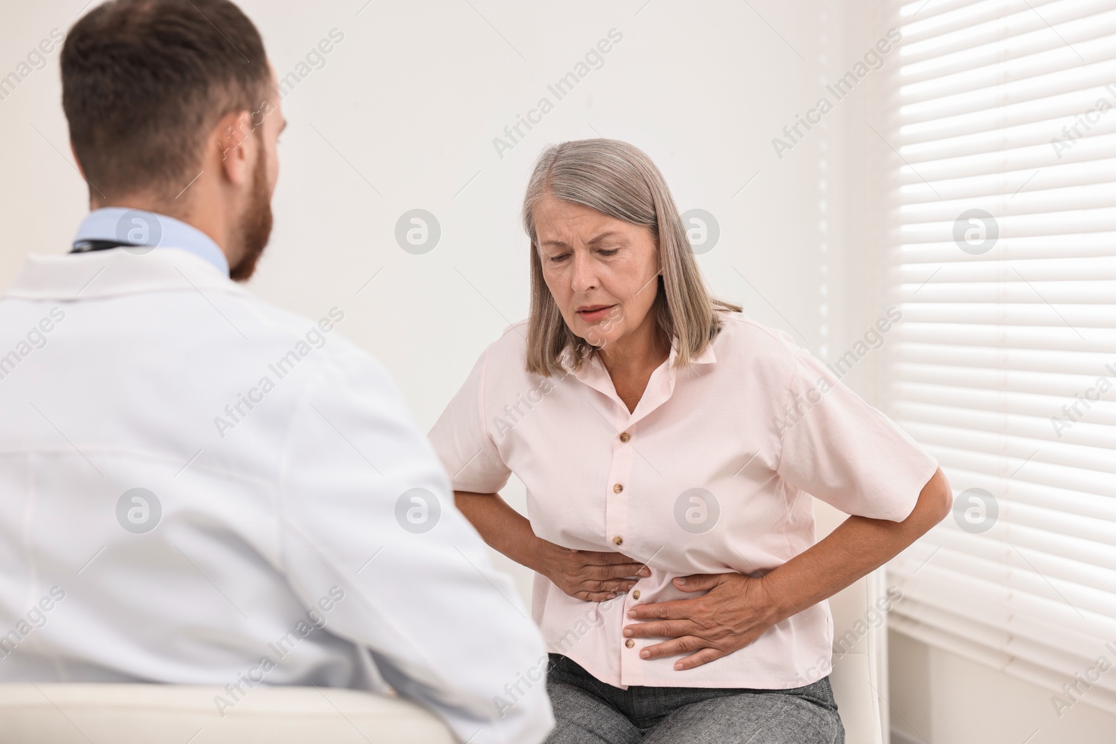 Photo of Doctor consulting senior patient with stomach pain in clinic, back view