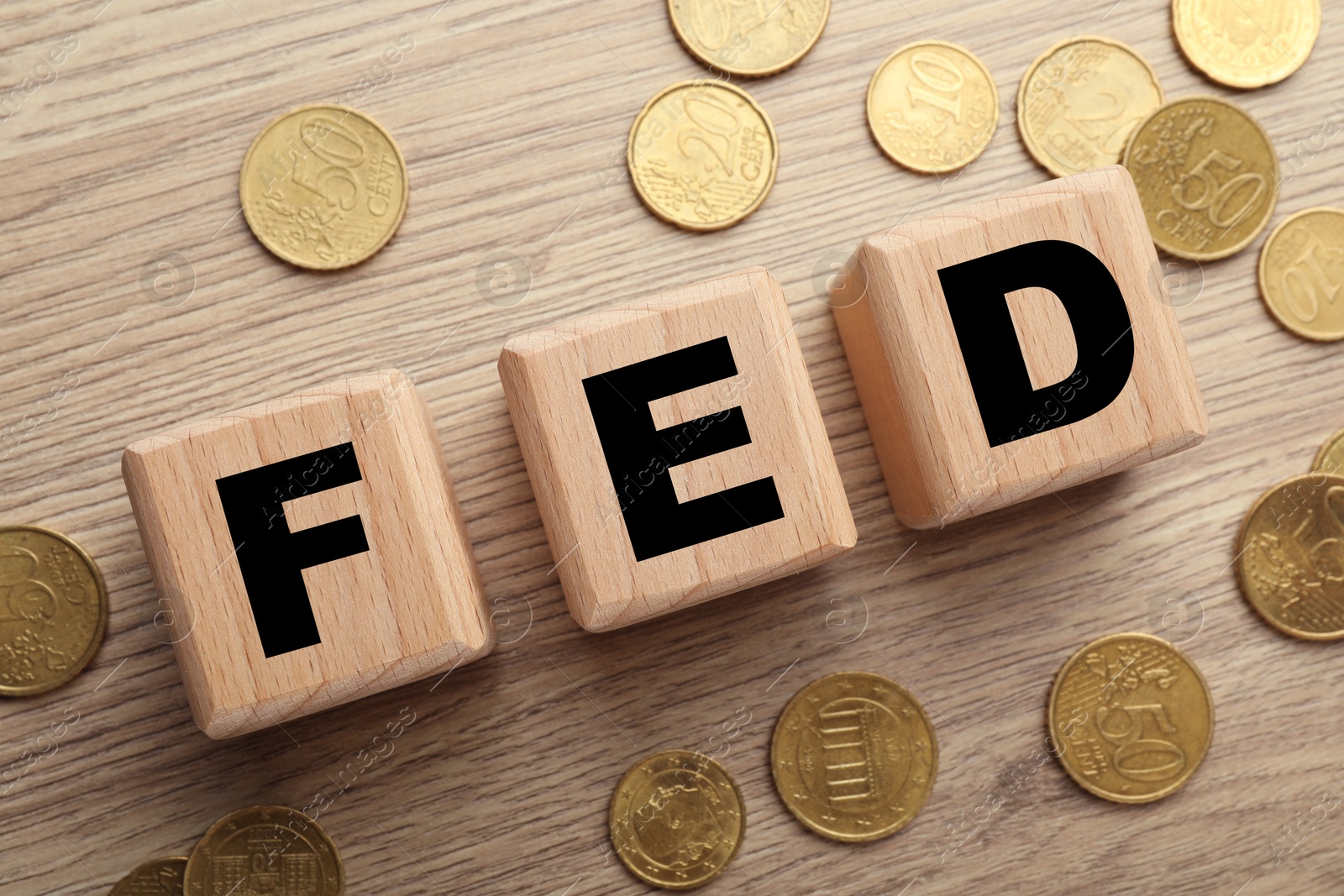 Photo of Cubes with letters Fed (Federal Reserve System) and coins on wooden table, flat lay