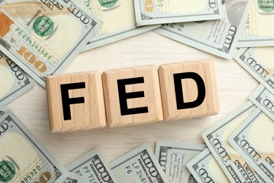 Photo of Cubes with letters Fed (Federal Reserve System) and dollar banknotes on white wooden table, flat lay