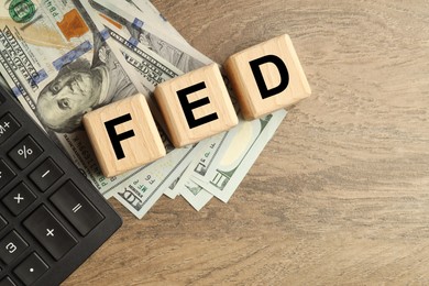 Photo of Cubes with letters Fed (Federal Reserve System), dollar banknotes and calculator on wooden table, flat lay