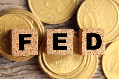 Photo of Cubes with letters Fed (Federal Reserve System) and coins on wooden table, flat lay