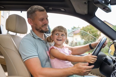 Photo of Happy man with his daughter holding steering wheel inside car