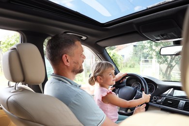 Man with daughter holding steering wheel inside car