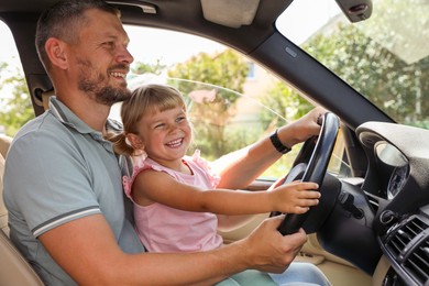 Photo of Happy man with his daughter holding steering wheel inside car