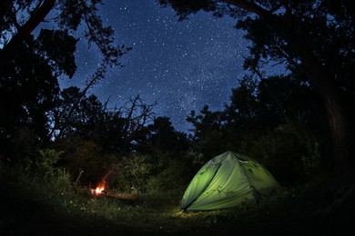 Photo of Modern camping tent and bonfire in forest at night. Fisheye lens effect