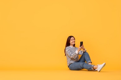 Photo of Smiling young woman using smartphone on yellow background. Space for text