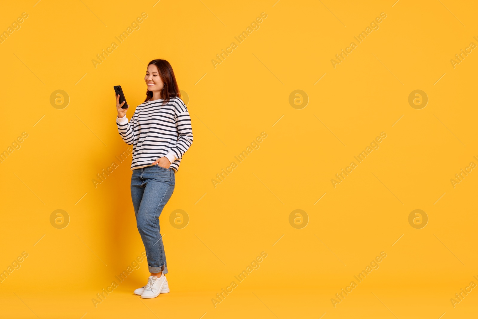 Photo of Smiling young woman using smartphone on yellow background. Space for text