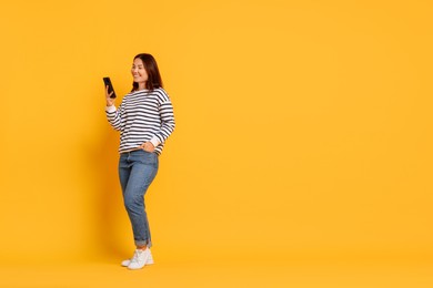 Photo of Smiling young woman using smartphone on yellow background. Space for text