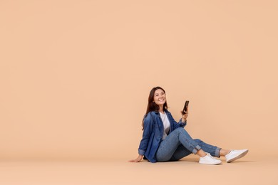 Photo of Smiling woman with smartphone on beige background. Space for text