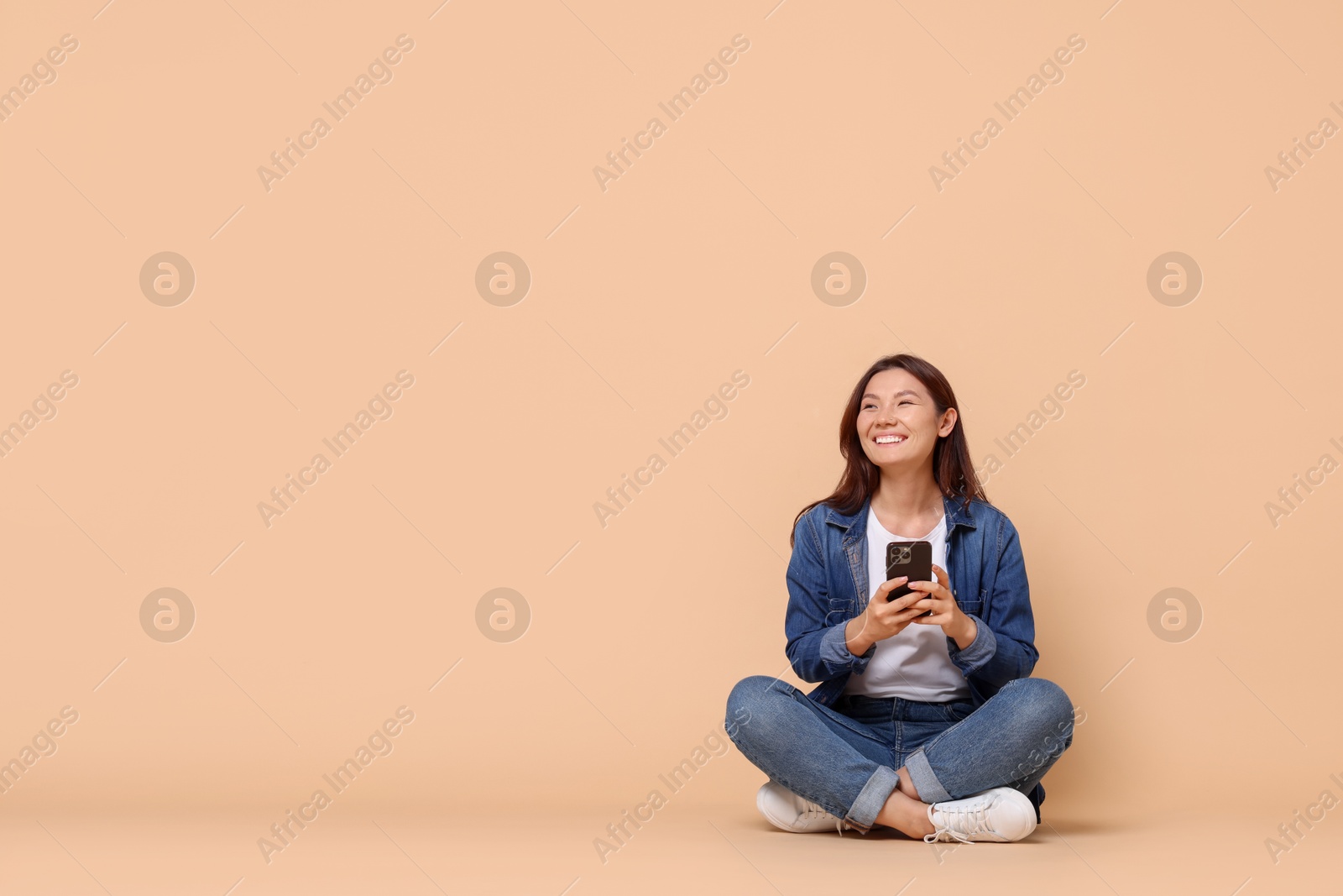 Photo of Smiling woman with smartphone on beige background. Space for text