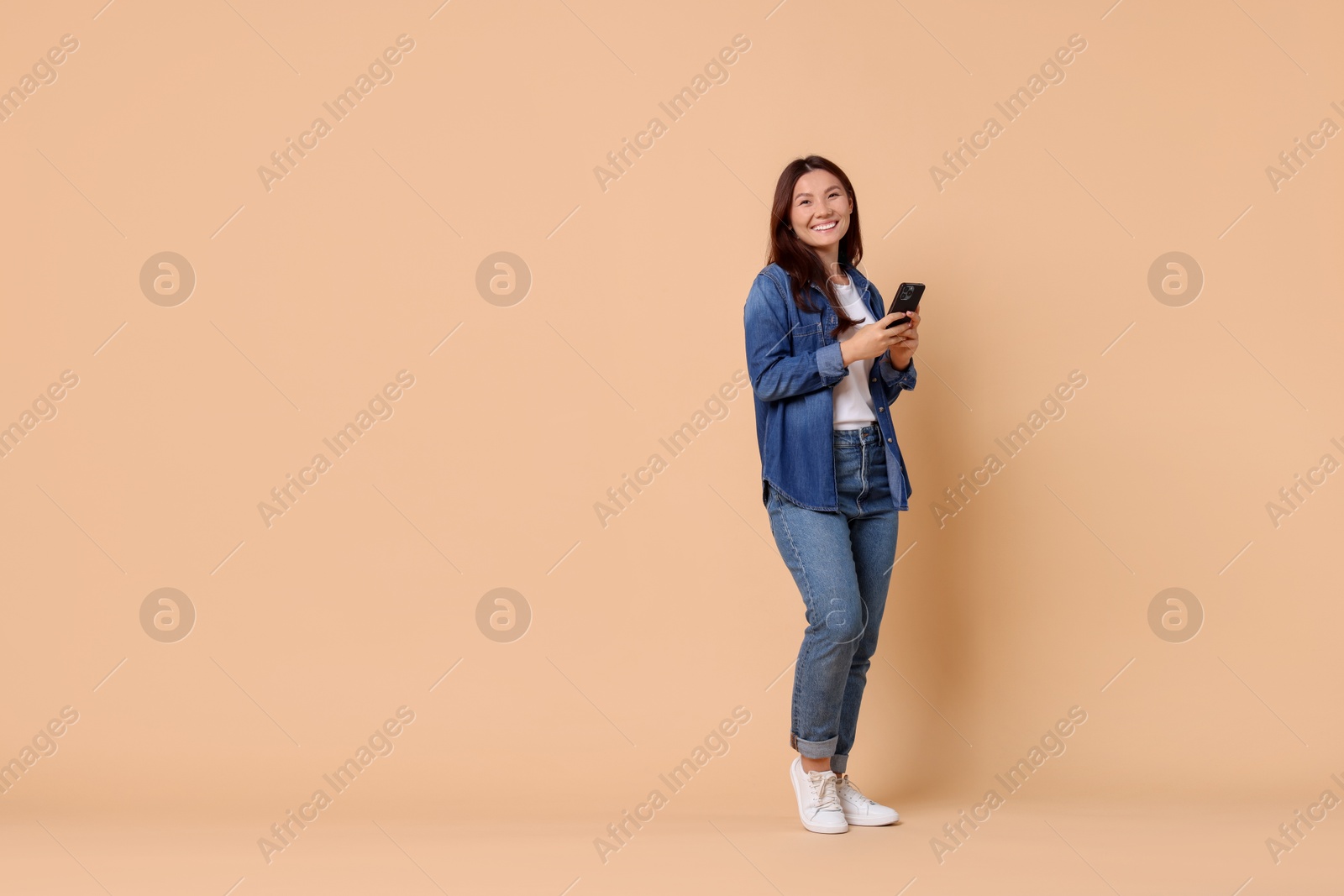 Photo of Smiling woman with smartphone on beige background. Space for text