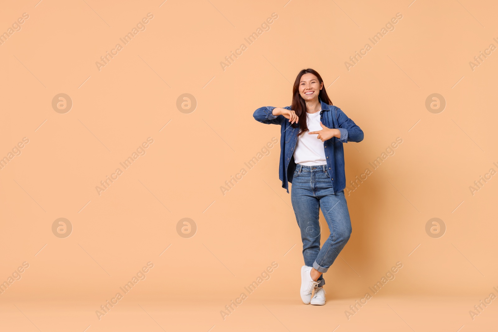 Photo of Smiling woman pointing at something on beige background. Space for text