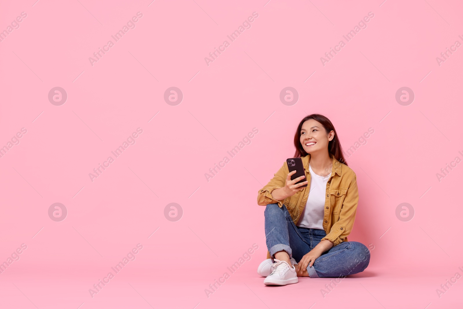 Photo of Smiling young woman with smartphone on pink background. Space for text