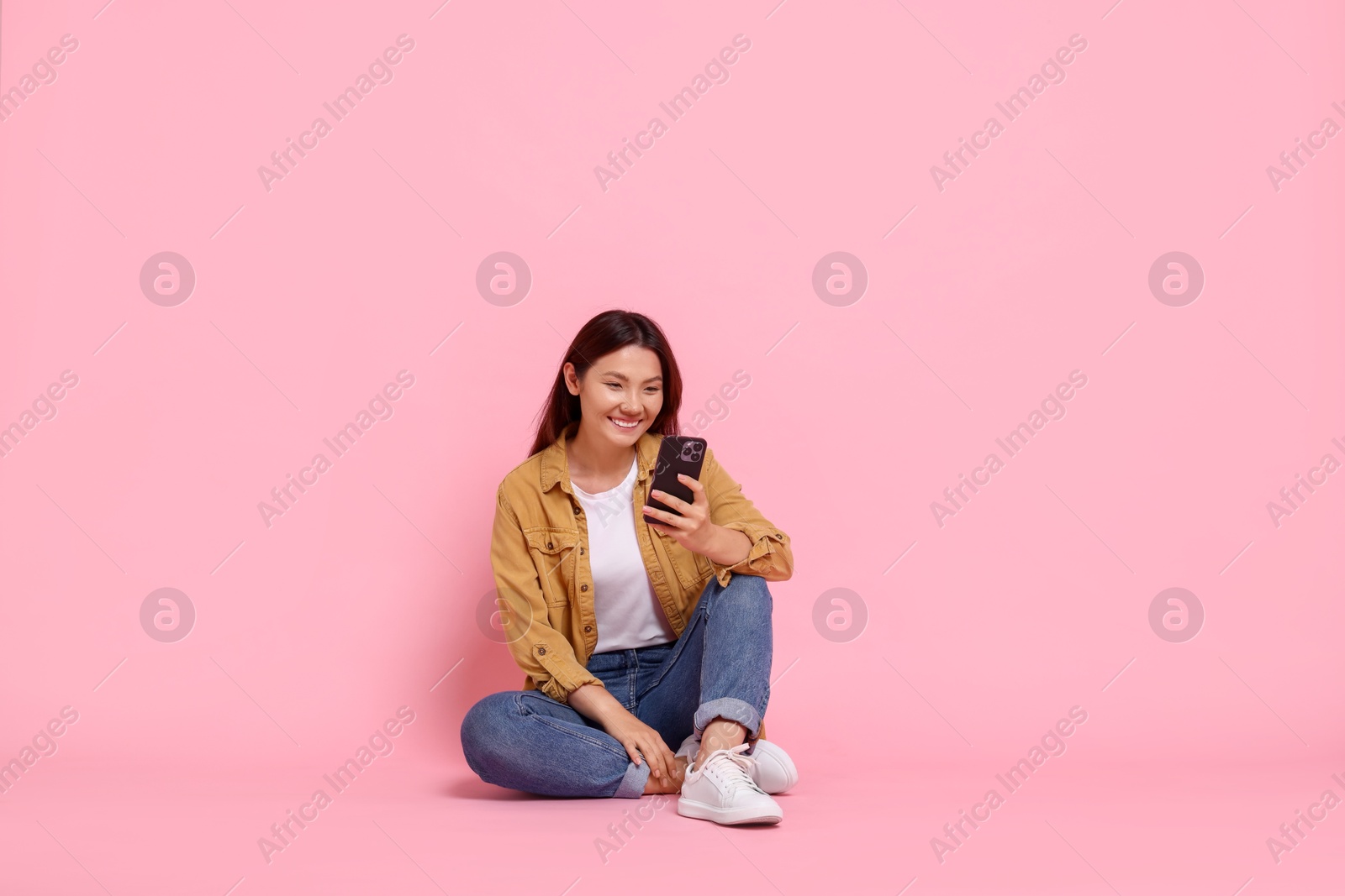 Photo of Smiling woman using smartphone on pink background