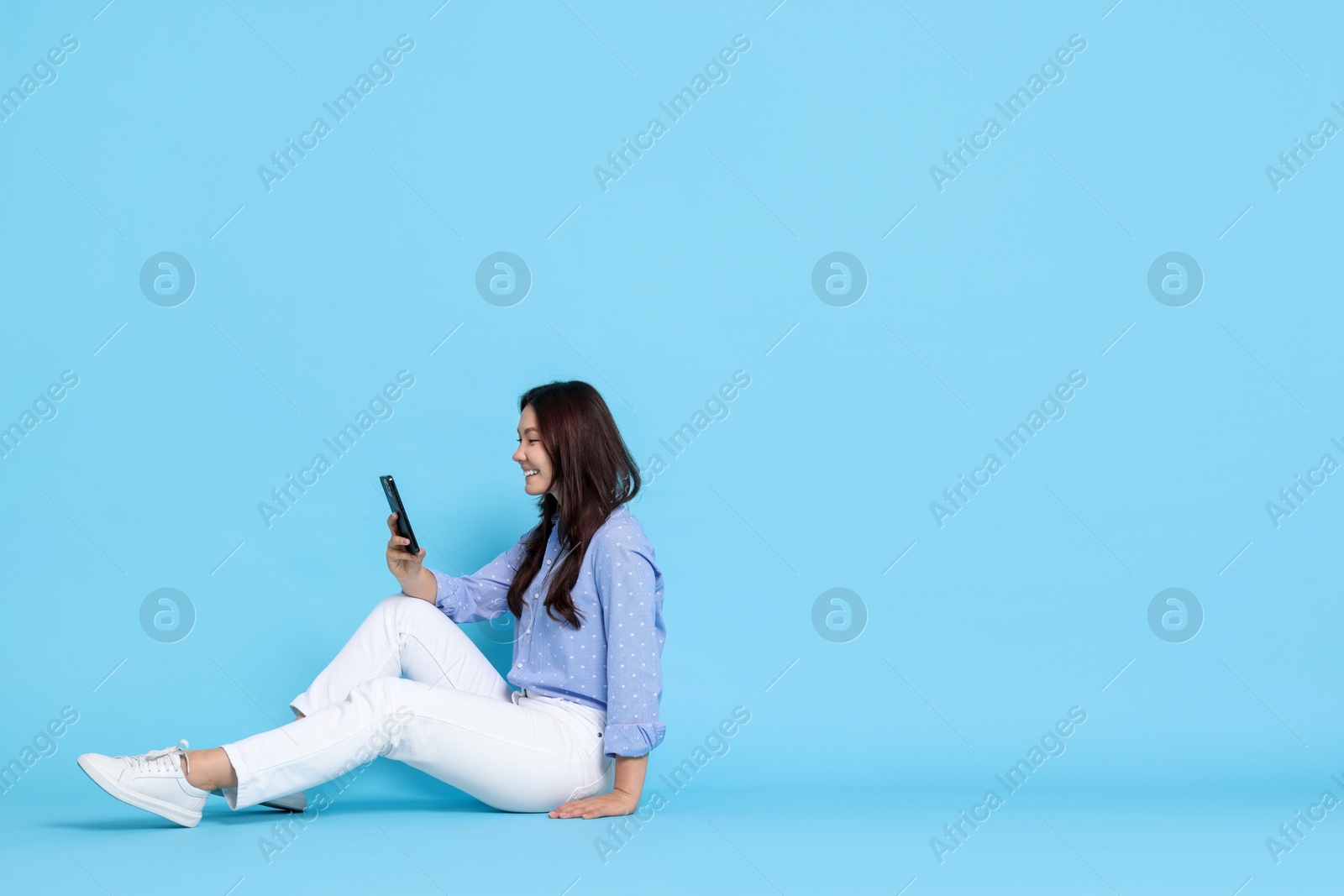 Photo of Smiling woman using smartphone on light blue background. Space for text