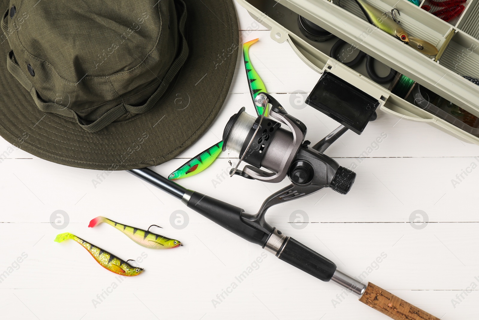 Photo of Fishing rod with spinning reel, hat, baits and tackle box on white wooden table, flat lay