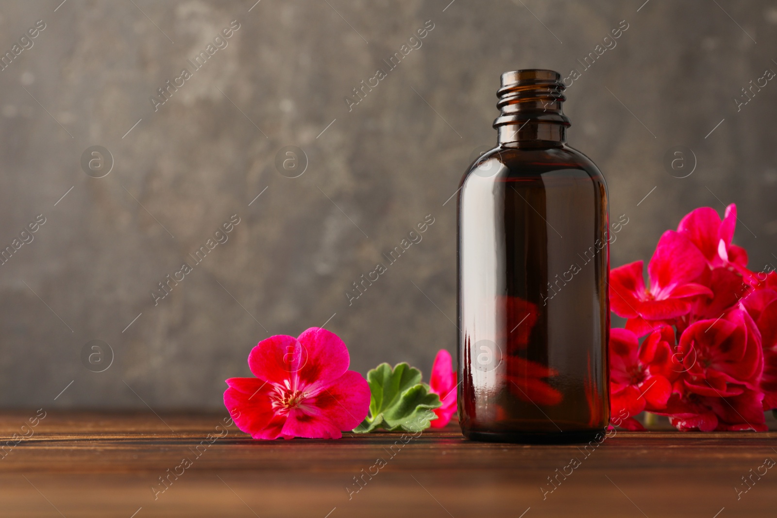 Photo of Geranium essential oil in bottle and beautiful flowers on wooden table