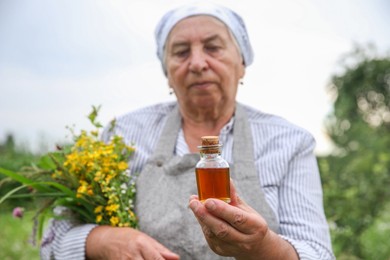 Senior woman with tincture and herbs outdoors, selective focus