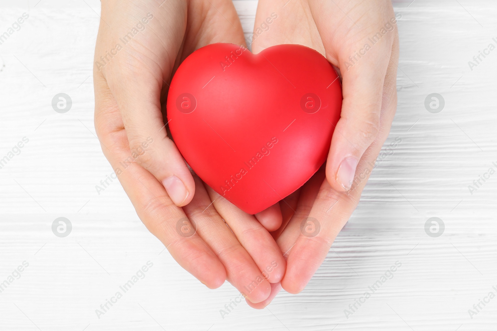 Photo of Woman holding red heart on white wooden background, top view