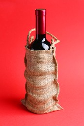 Photo of Wine bottle in burlap bag on red background