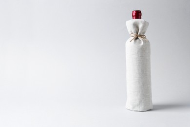 Photo of Wine bottle in burlap package on light grey background, space for text