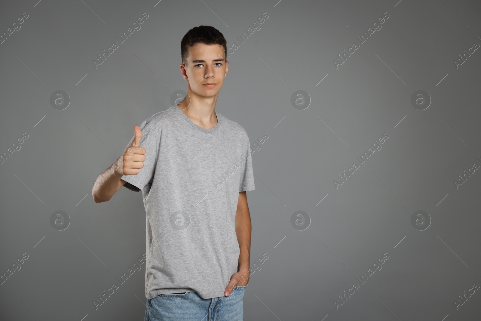 Photo of Teenage boy wearing t-shirt and showing thumbs up on grey background, space for text