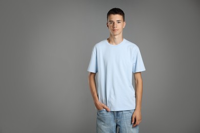 Teenage boy wearing light blue t-shirt on grey background, space for text