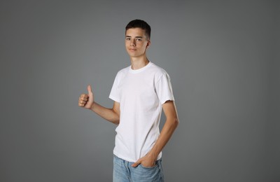 Teenage boy wearing white t-shirt and showing thumbs up on grey background