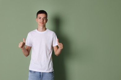 Photo of Teenage boy wearing white t-shirt and showing thumbs up on green background, space for text