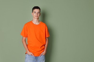 Photo of Teenage boy wearing orange t-shirt on green background, space for text