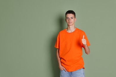 Photo of Teenage boy wearing orange t-shirt and showing thumbs up on green background, space for text