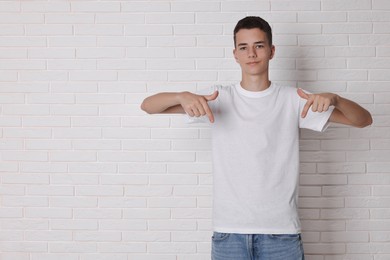 Teenage boy wearing t-shirt near white brick wall, space for text