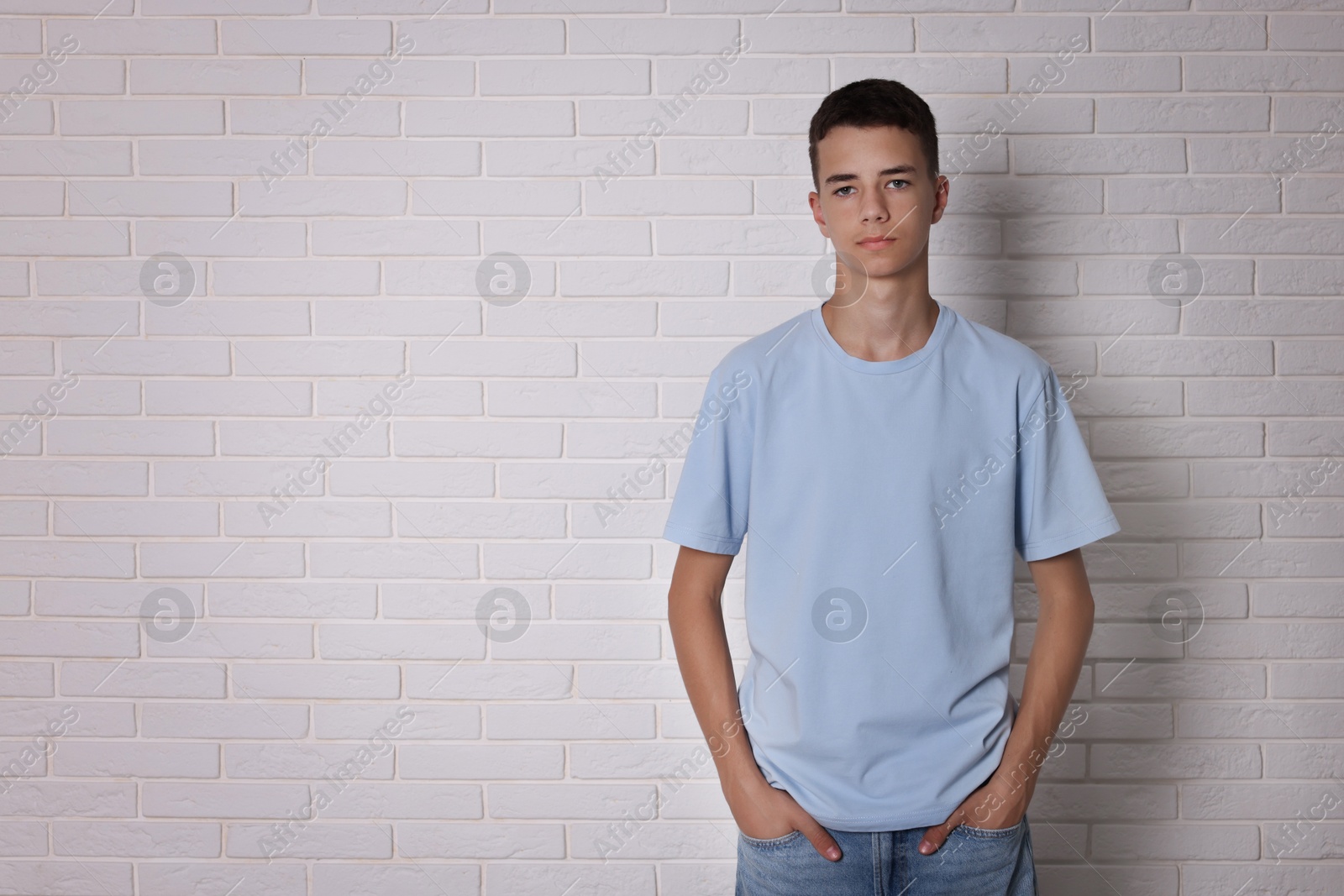 Photo of Teenage boy wearing light blue t-shirt near white brick wall, space for text