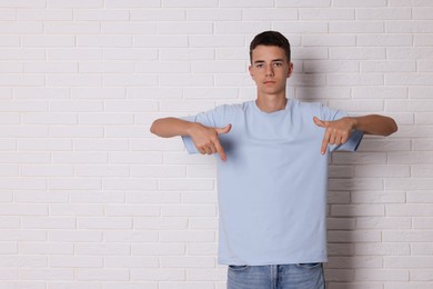 Teenage boy wearing light blue t-shirt near white brick wall, space for text