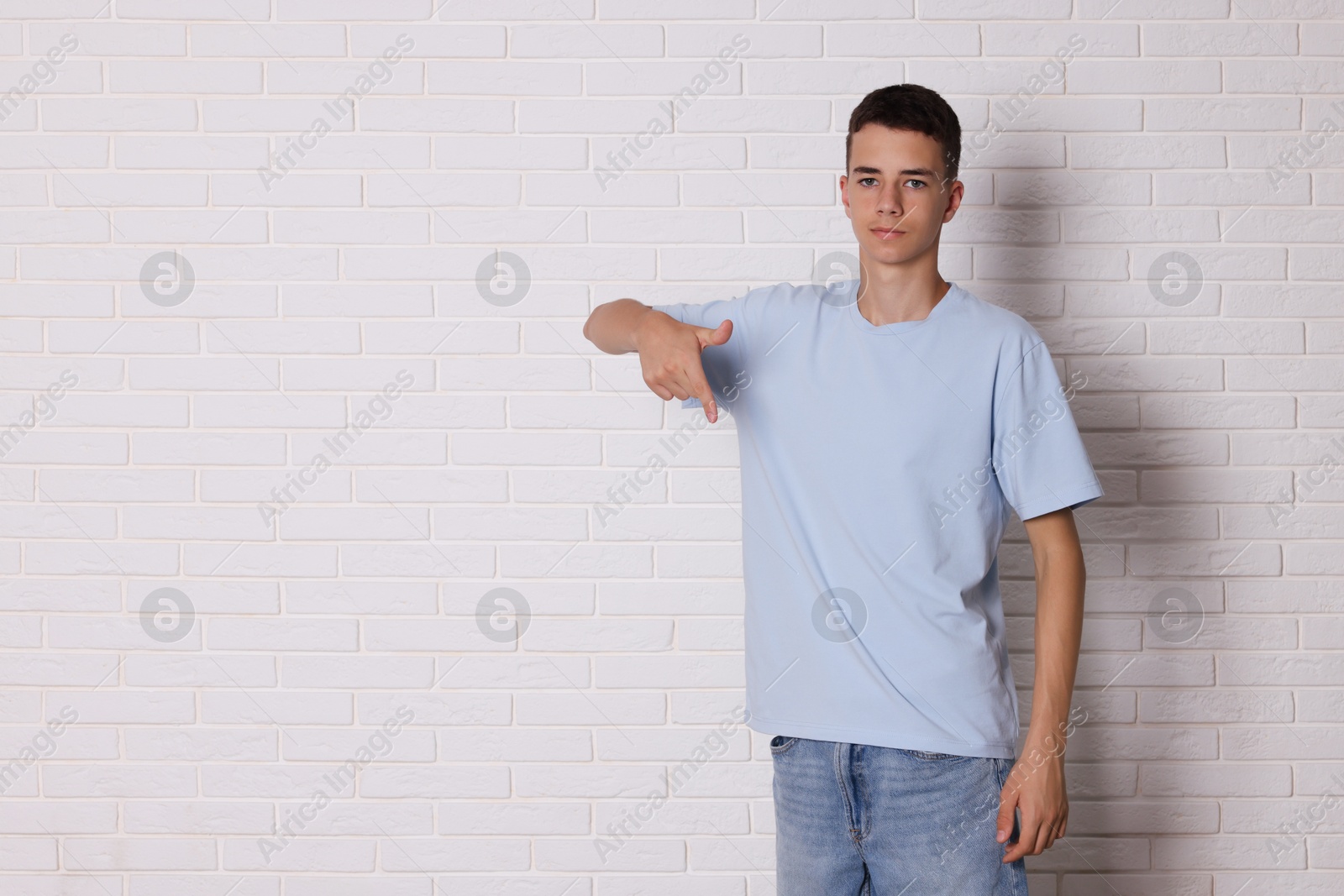 Photo of Teenage boy wearing light blue t-shirt near white brick wall, space for text