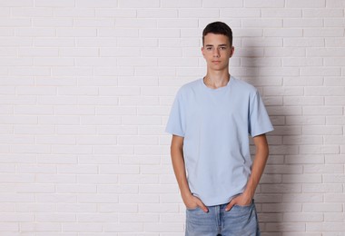 Teenage boy wearing light blue t-shirt near white brick wall, space for text