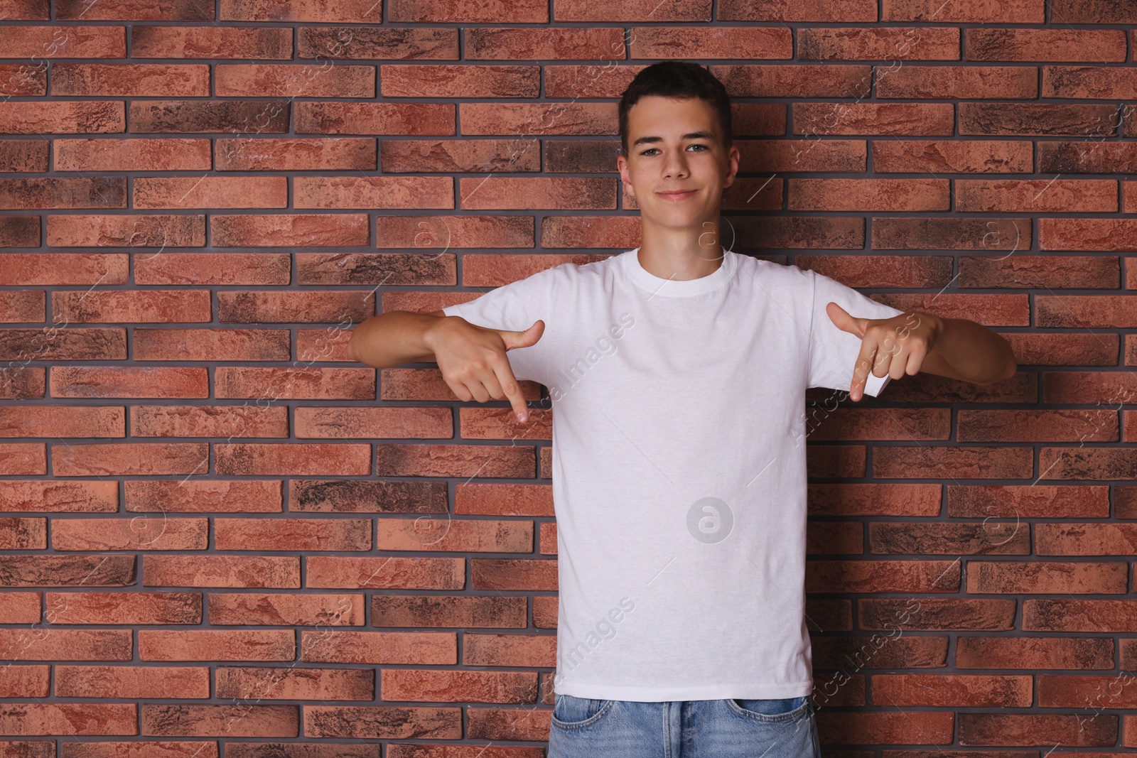 Photo of Teenage boy wearing white t-shirt near brick wall, space for text