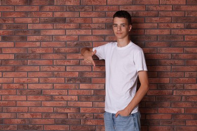 Teenage boy wearing white t-shirt near brick wall, space for text