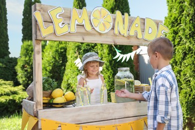 Photo of Cute little girl selling natural lemonade to boy in park