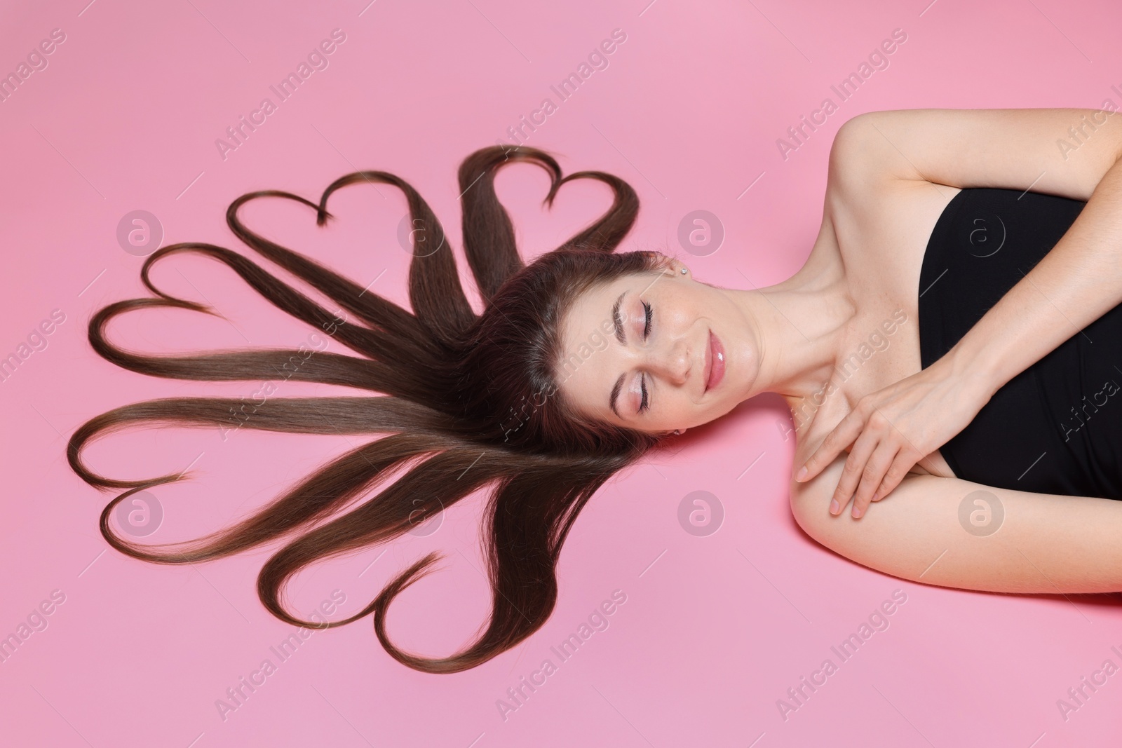 Photo of Beautiful young woman with hair in shape of hearts on pink background