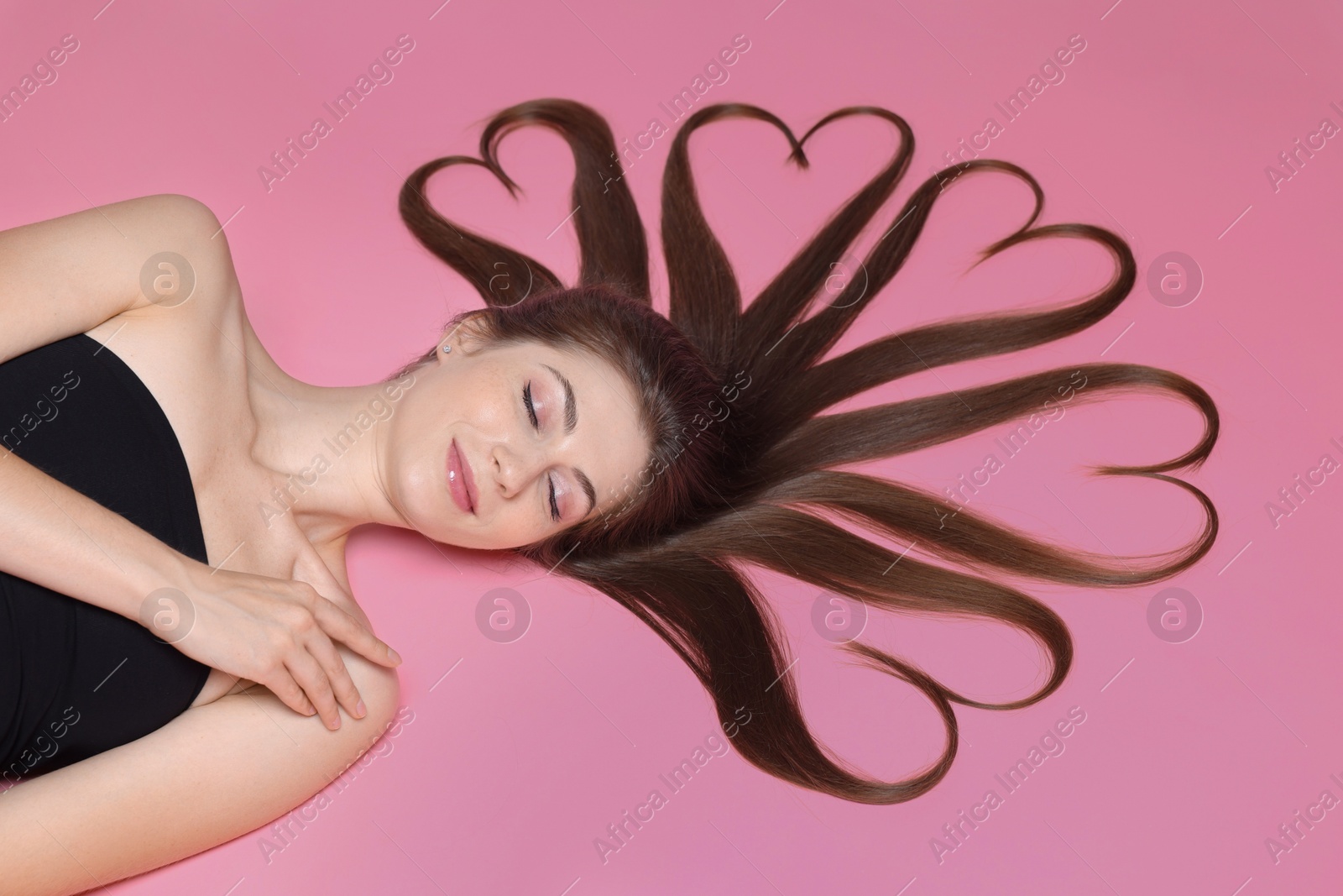 Photo of Beautiful young woman with hair in shape of hearts on pink background