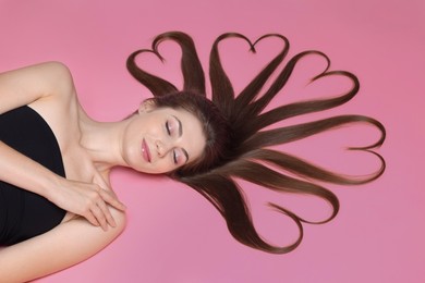 Photo of Beautiful young woman with hair in shape of hearts on pink background